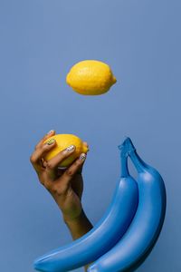 Close-up of hand holding fruit against blue sky
