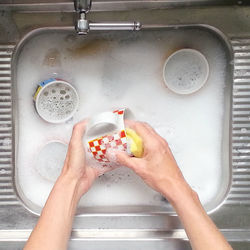 Cropped image of hands washing cups in sink