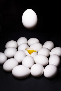 White chicken eggs with one broken egg and one in the air on a black background