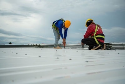 Asian construction workers are installing metal roofing sheets for industrial roof installations.