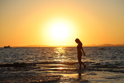 Silhouette woman standing on beach against sky during sunset