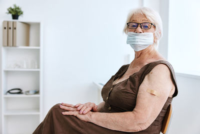 Portrait of senior woman wearing mask while sitting at hospital