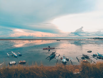 Boats moored in sea against sky during sunset