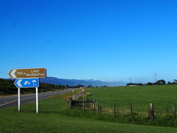 Road sign on field against clear blue sky