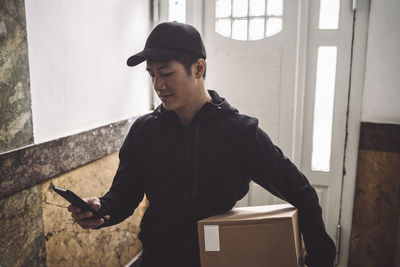 Delivery man using mobile phone while holding package against door