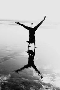 Silhouette woman doing cartwheel in sea against sky
