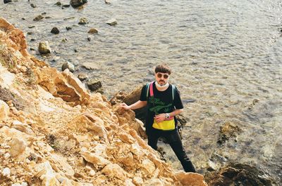 High angle portrait of man standing by rock against sea