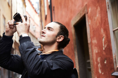 Close-up of young man with camera standing against buildings