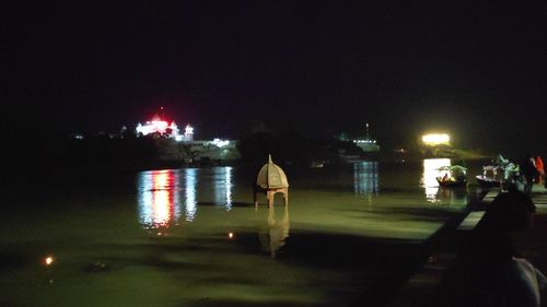 Illuminated buildings by river against sky at night