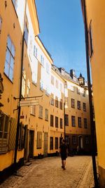 Rear view of woman walking on footpath amidst buildings in city