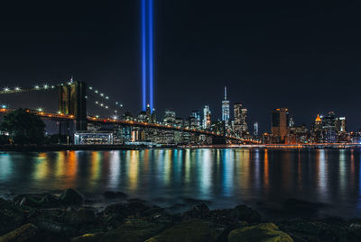 Illuminated buildings by river against sky at night