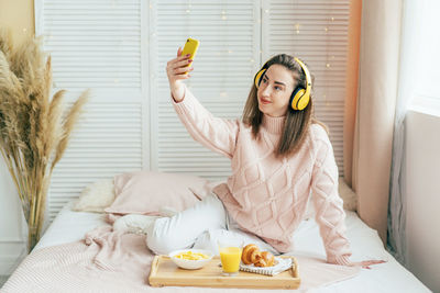 Woman doing selfie while sitting on bed by breakfast