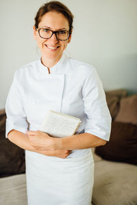 Female chef in uniform holding recipe notebook while smiling at camera