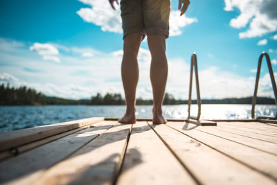 Low section of man standing on pier over lake against sky