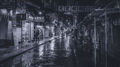 Woman with umbrella walking by wet street in city at night during rainy season