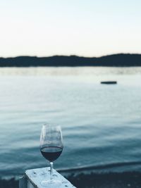 Close-up of wineglass by lake against clear sky