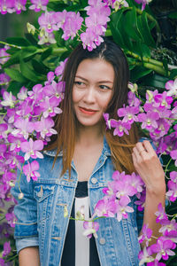 Portrait of beautiful young woman standing by pink flowering plants