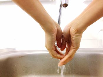 Close-up of woman washing hands below faucet in sink