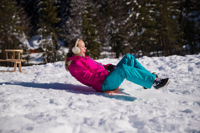 Side view of girl sledging on snow covered land