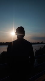 Rear view of silhouette man standing by lake against sky during sunset