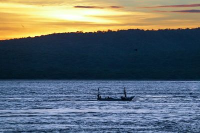 Silhouette boat sailing on sea against sky during sunset