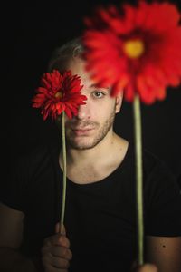 Close-up of woman with red flower against black background