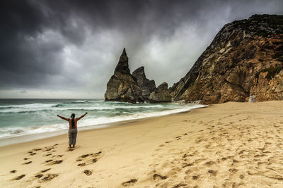 Rear view of man standing with arms outstretched at beach against sky