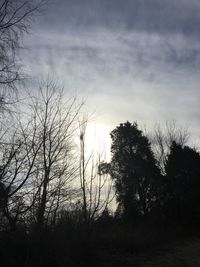 Low angle view of bare trees against cloudy sky