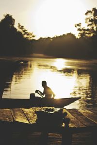 Silhouette of man sitting on lake at sunset