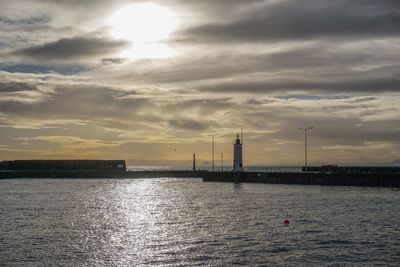 Silhouette factory by river against sky during sunset