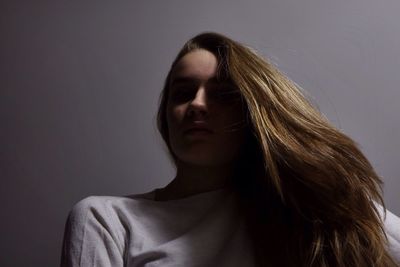 Low angle view of young woman with long blond hair against gray background