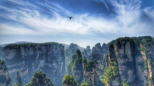 Low angle view of airplane flying over mountain against sky