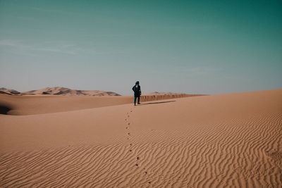 Rear view of man walking on sand dune in desert