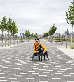 Smiling young woman in yellow hoodie hugging fluffy shaggy gray dog on alley, pet love, walking dog