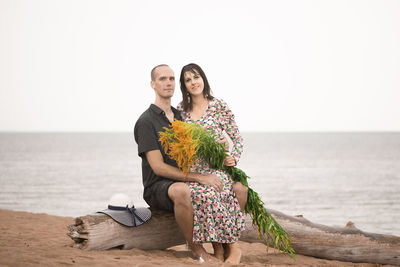 Young romantic couple sitting by the sea and looking to camera
