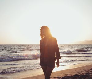 Rear view of woman standing on beach against clear sky