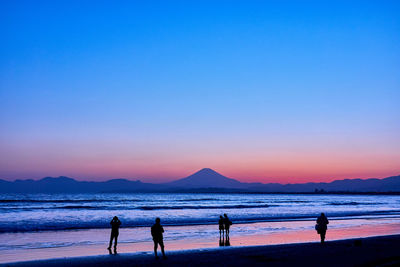 Silhouette people on beach against sky during sunset