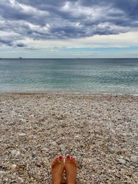 Low section of woman relaxing on beach against cloudy sky