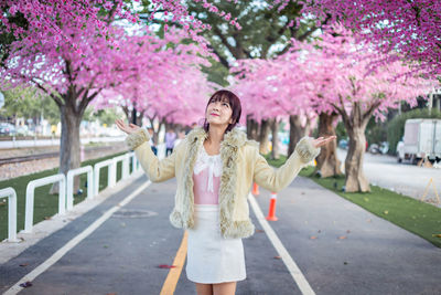 Woman standing by pink flower tree in city