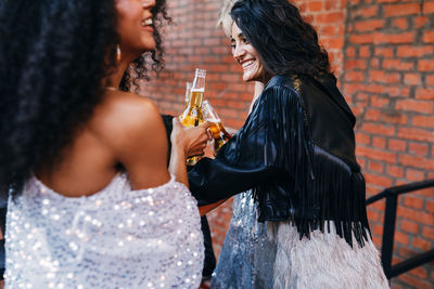 Friends holding beer bottles while standing against wall