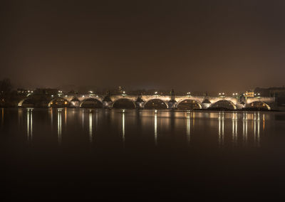 Illuminated buildings by river against sky at night