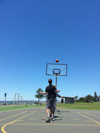 Friends playing basketball on court against clear blue sky during sunny day