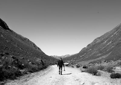 Rear view of man walking on mountain against clear sky