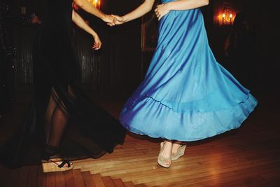 Low section of female friends dancing on hardwood floor