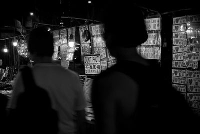 Rear view of people standing on illuminated street at night