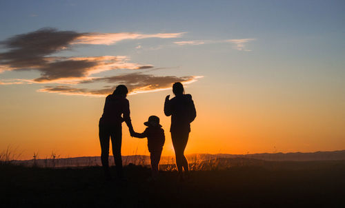 Silhouette women and boy on field against sky during sunset