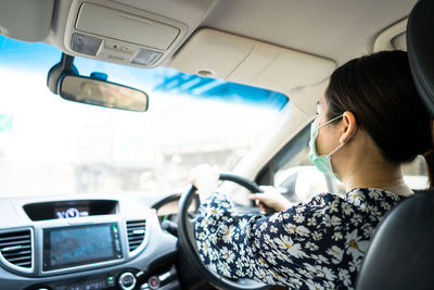 Young woman wearing medical face mask to preventing flu, pollution and convid 19 while driving.