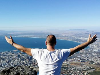 Rear view of man with arms outstretched standing against sea and sky on sunny day