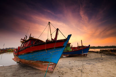 Boat moored on beach against sky during sunset