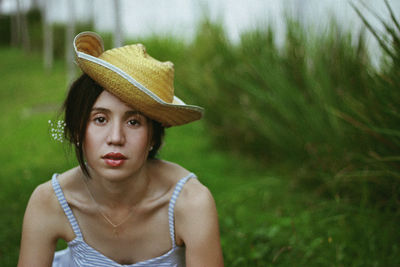 Portrait of woman wearing hat while sitting on field